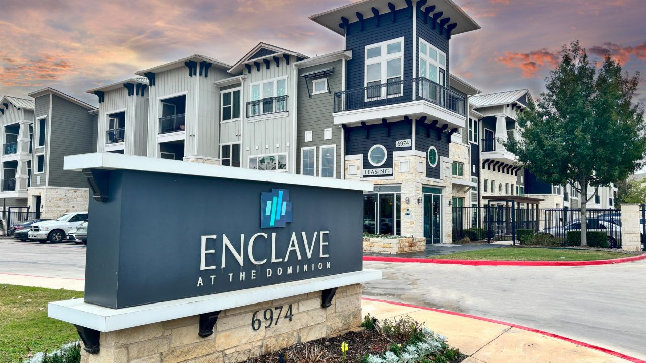 Enclave at the Dominion apartments modern apartment complex with "Enclave at the Dominion" sign in front, under a dramatic sunset sky.