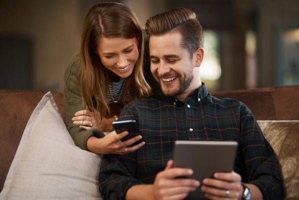 Enclave at the Dominion A smiling couple on a couch, looking at a smartphone and a tablet together.