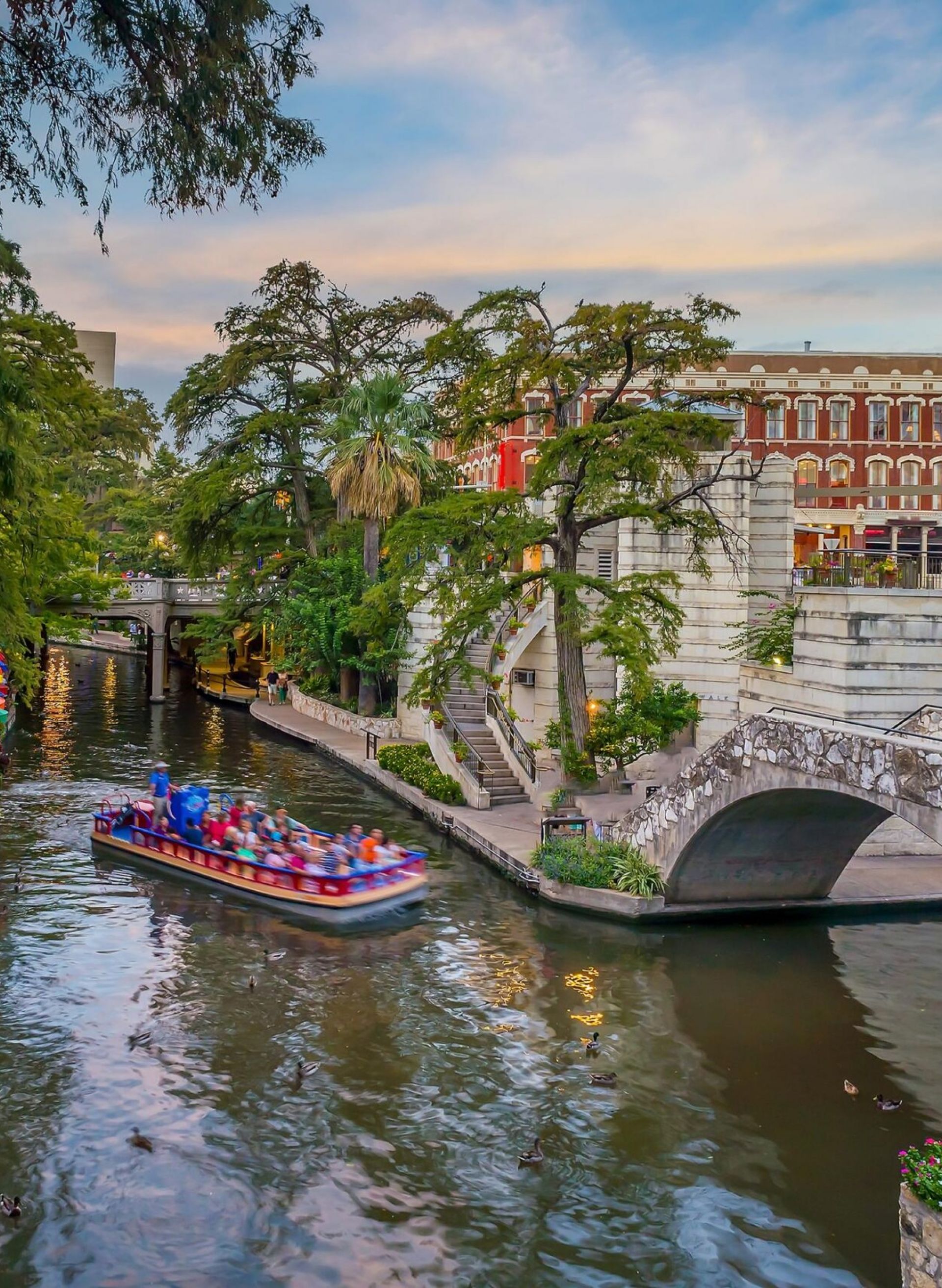 Enclave at the Dominion Colorful umbrellas line the San Antonio River Walk as a boat passes under a stone bridge.