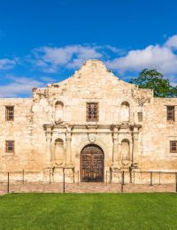 Enclave at the Dominion The historic Alamo building with a Texas flag and lush green lawn under a clear blue sky.