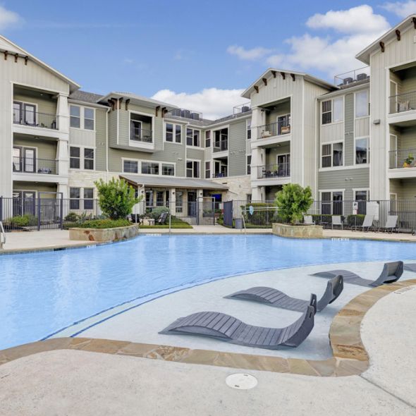 Enclave at the Dominion Apartments A modern apartment complex with a pool, lounge chairs, and beige and green exterior under a blue sky.